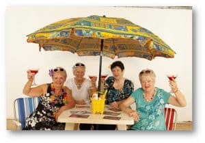 A group of older women enjoy drinks under a beach umbrella